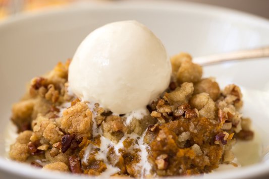 Closeup photo of a white dish of Easy Pumpkin Praline Cobbler with a scoop of ice cream on top.
