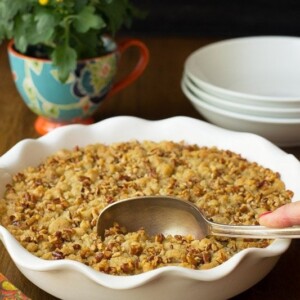 Vertical picture of Easy Pumpkin Praline Cobbler in a pie pan with flowers and white bowls in the background