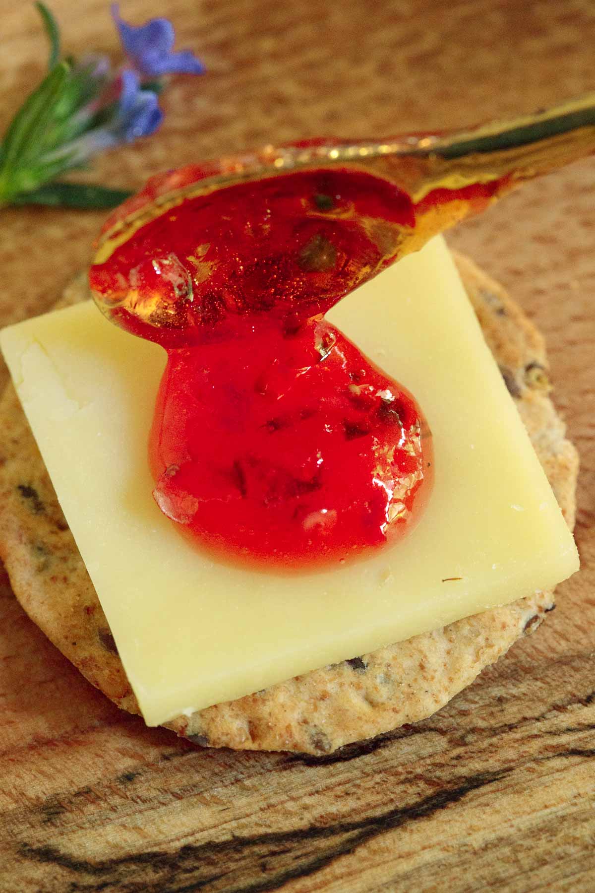 A photo of Easy Strawberry Jalapeño Jam on a cracker over a slice of cheese.