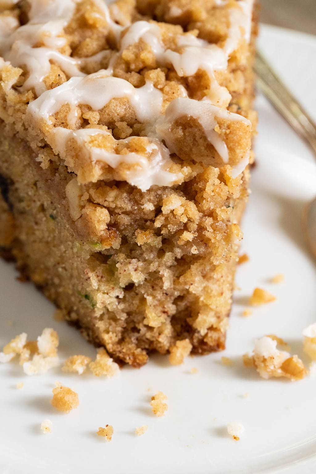 Extreme closeup vertical photo of the wedge front of a slice of Easy Zucchini Crumb Cake on a white serving plate.