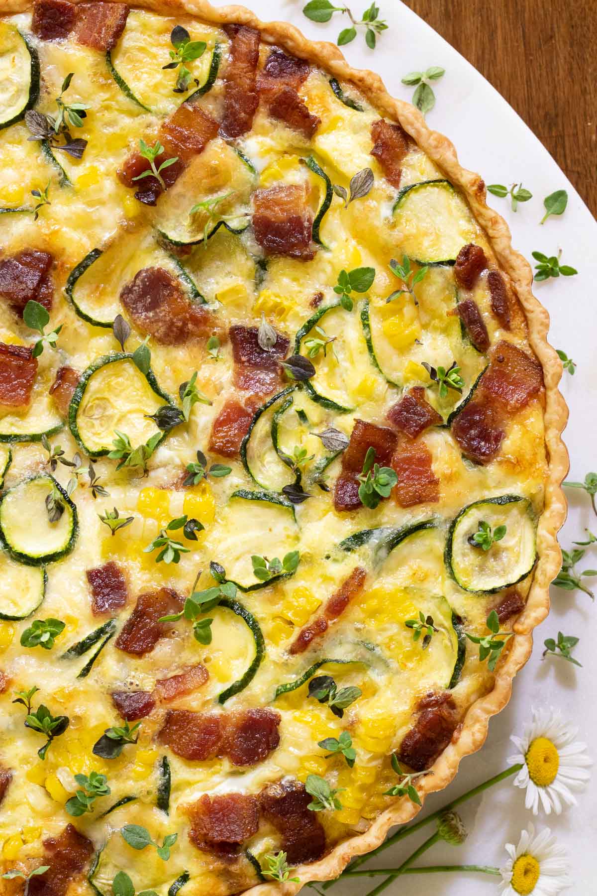 Closeup vertical photo of an Easy Zucchini Summer Quiche on a white serving plate garnished with thyme leaves.