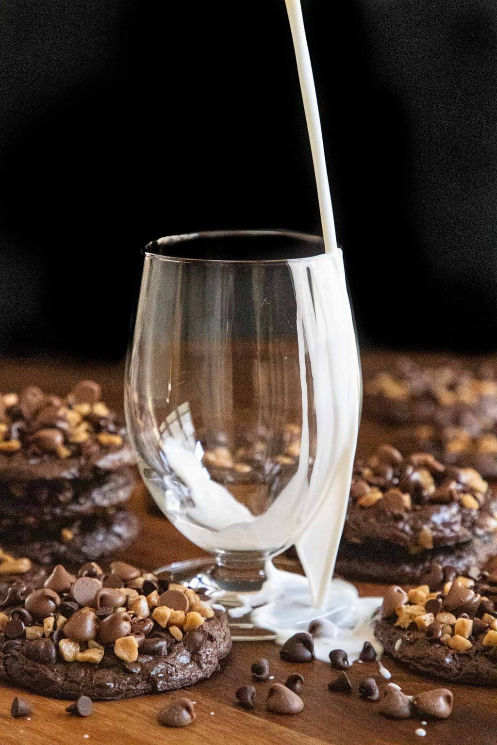 Vertical "oops" photo of milk spilling out over a glass surrounded by Flourless Toffee Chocolate Cookies .