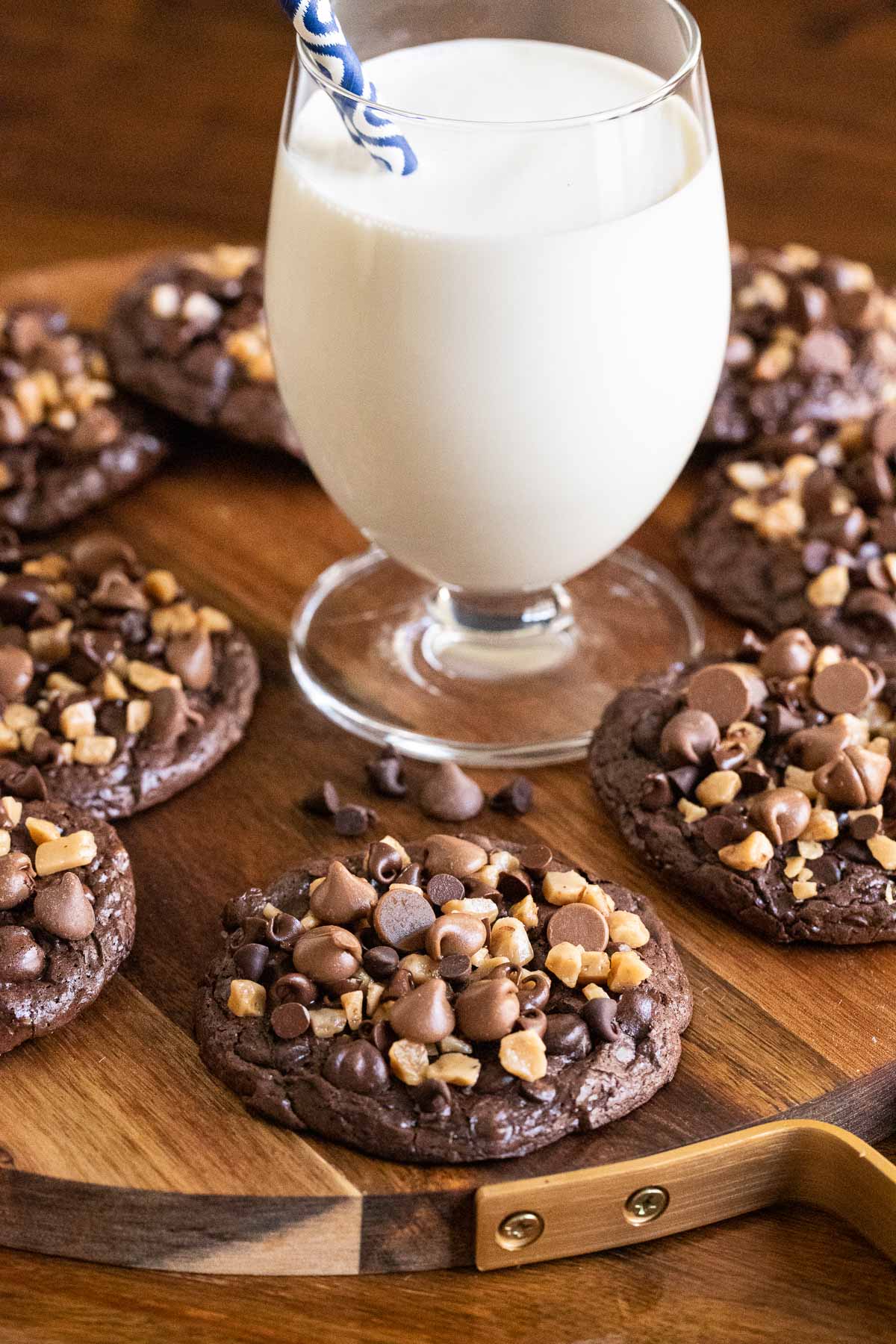 Vertical photo of a wood platter filled with Flourless Toffee Chocolate Cookies with a glass of milk in the center.