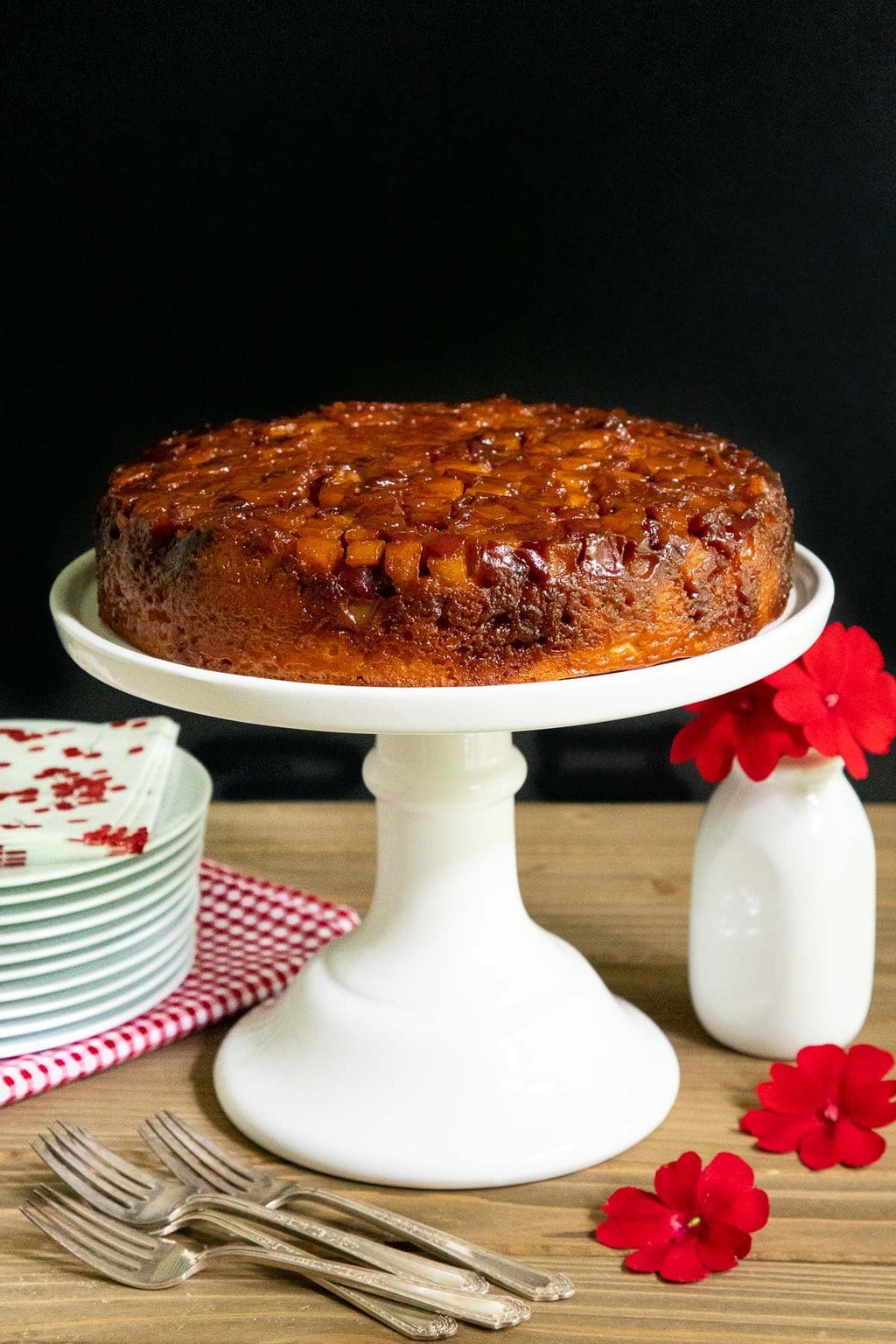 Vertical photo of a French Caramel Apple Cake on a white pedestal cake stand against a black background.