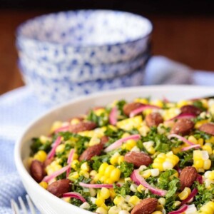 Vertical picture of Fresh Corn Kale Salad in a white bowl with blue and white bowls in the background