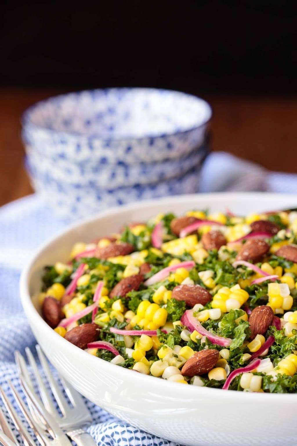 Vertical photo of Fresh Corn Kale Salad in a white serving bowl with blue and white individual serving bowls in the background.
