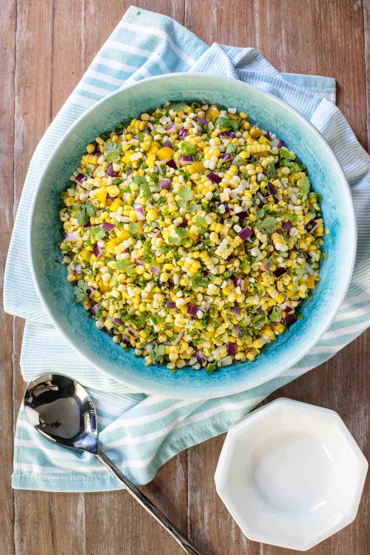 Overhead photo of a turquoise serving bowl of Fresh Corn Salad with a patterned cloth underneath on a distressed wood table.