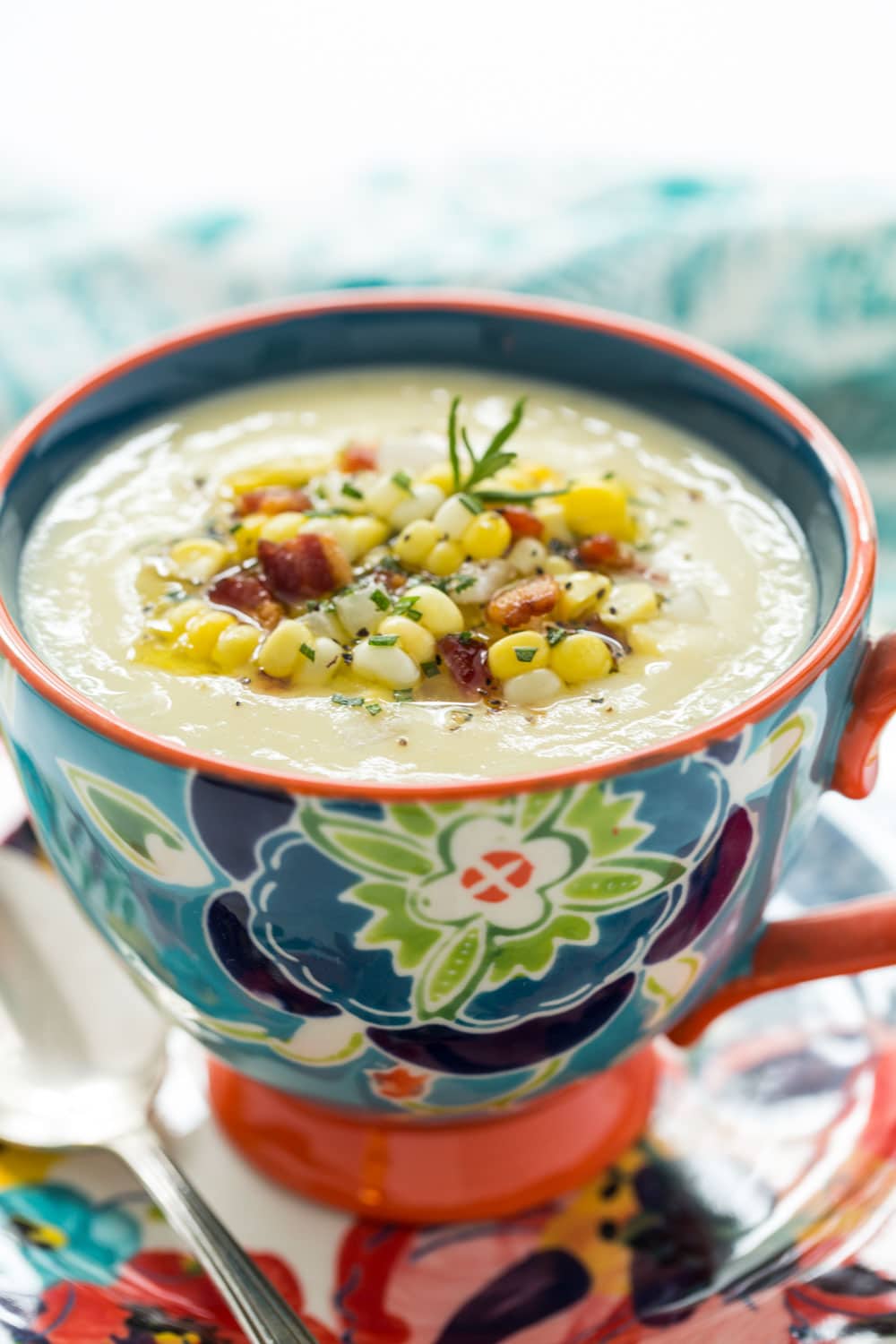 Vertical closeup photo of Fresh Corn Soup in a floral patterned mug and plate.