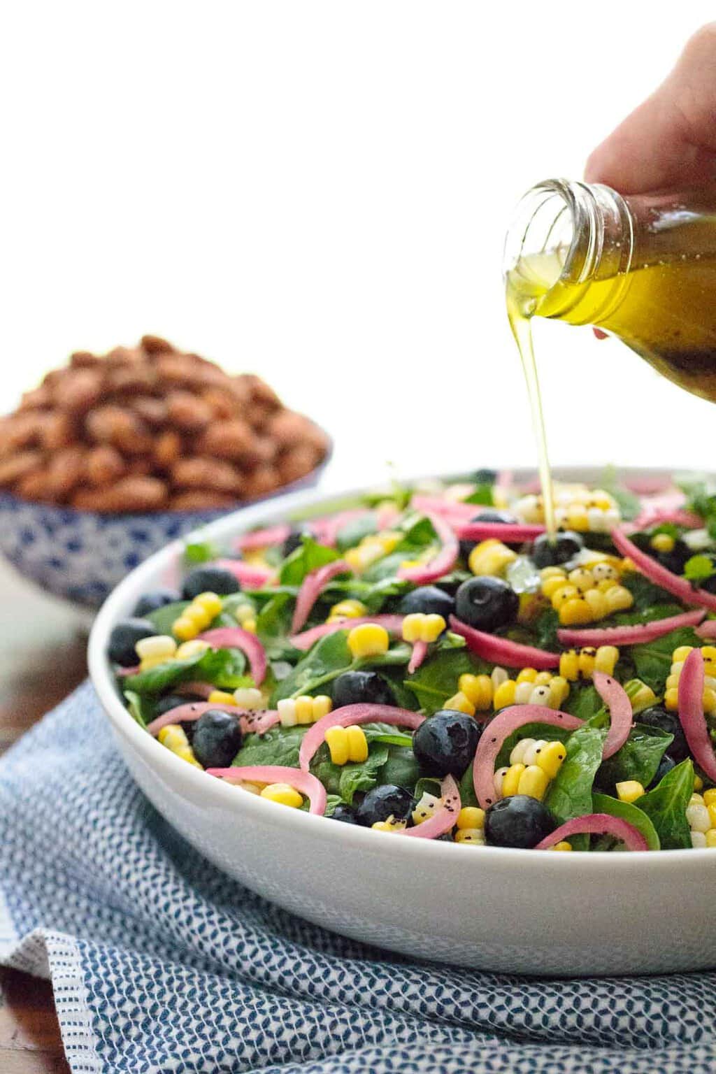 Vertical picture of Blueberry Spinach Salad with fresh corn in a white bowl with dressing poured on top