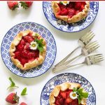Overhead picture of mini fresh strawberry galettes on blue and white plates