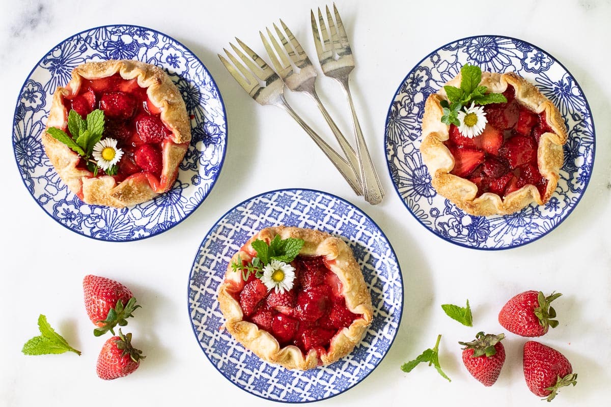 Overhead horizontal photo of three serving plates of Fresh Strawberry Galettes on a white marble countertop.