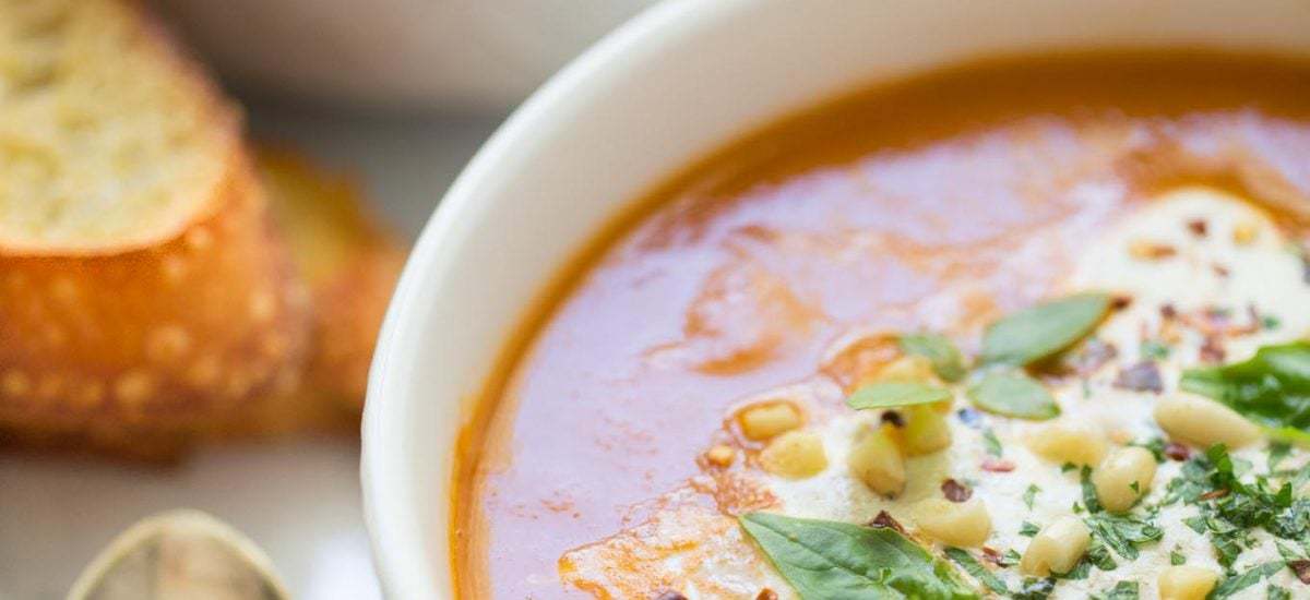 Fresh Tomato Basil Soup - thecafesucrefarine.com Overhead medium closeup shot of Fresh Tomato Basil Soup garnished with basil leaves, pine nuts and cheese