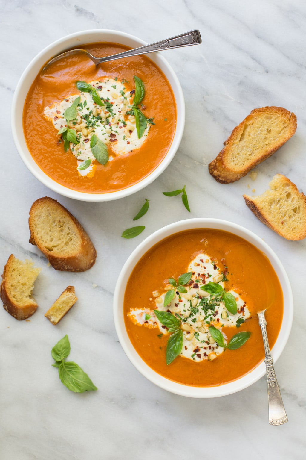 Overhead photo of two bowls of Fresh Tomato Basil Soup surrounded by fresh basil leaves and french bread.
