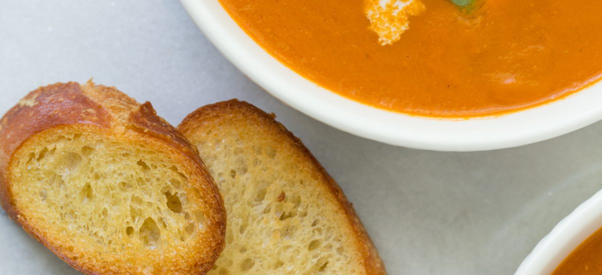 Fresh Tomato Basil Soup - thecafesucrefarine.com Tight overhead closeup of two bowls of Fresh Tomato Basil Soup garnished with basil leaves, pine nuts and mozzarella cheese Crusty bread and spoons sit along side the bowls.