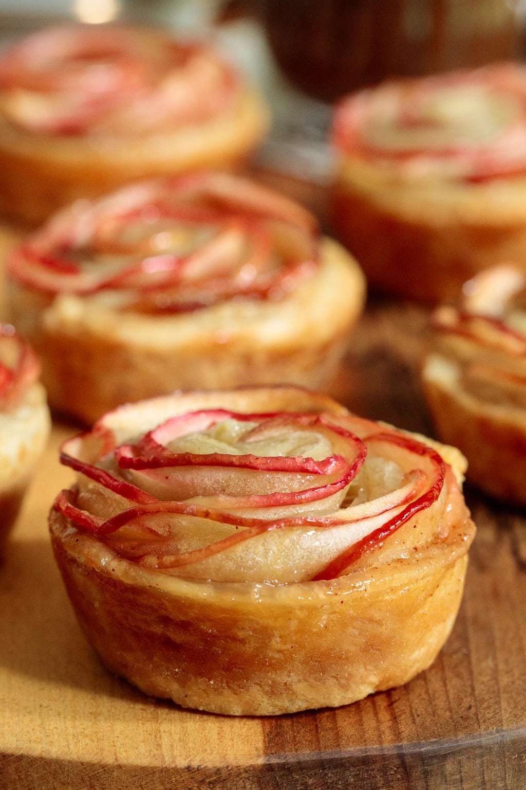 Photo of a batch of Glazed Puff Pastry Apple Roses on a wood board.