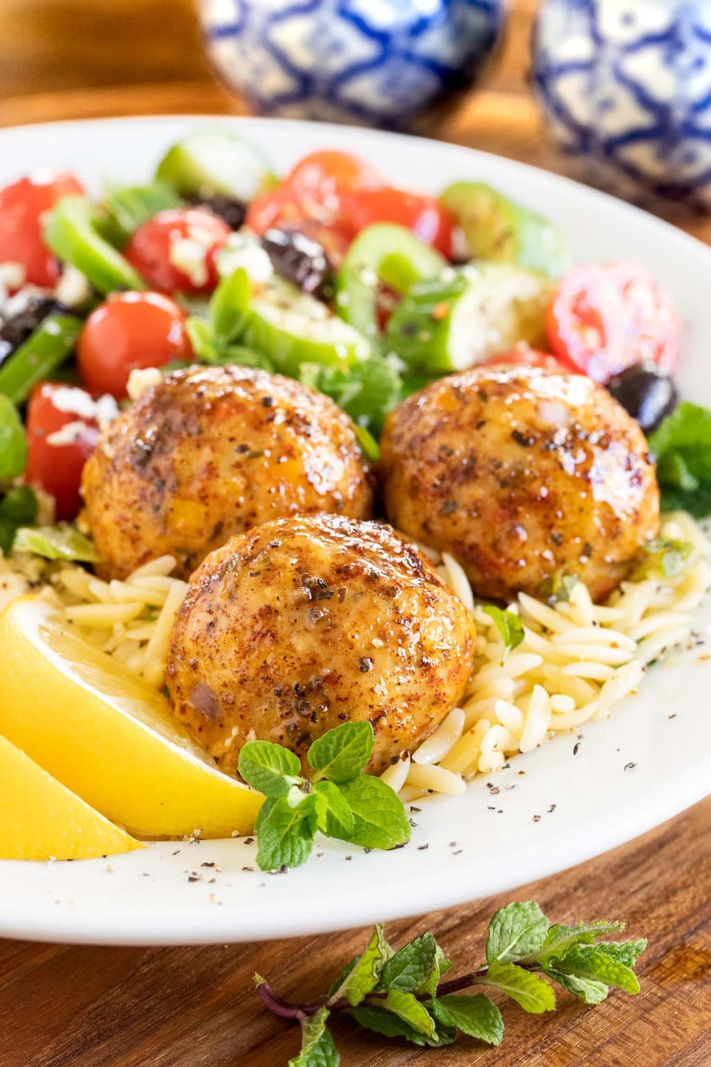 Close up vertical photo of Greek Chicken Meatballs in a bed of orzo pasta and fresh vegetables.