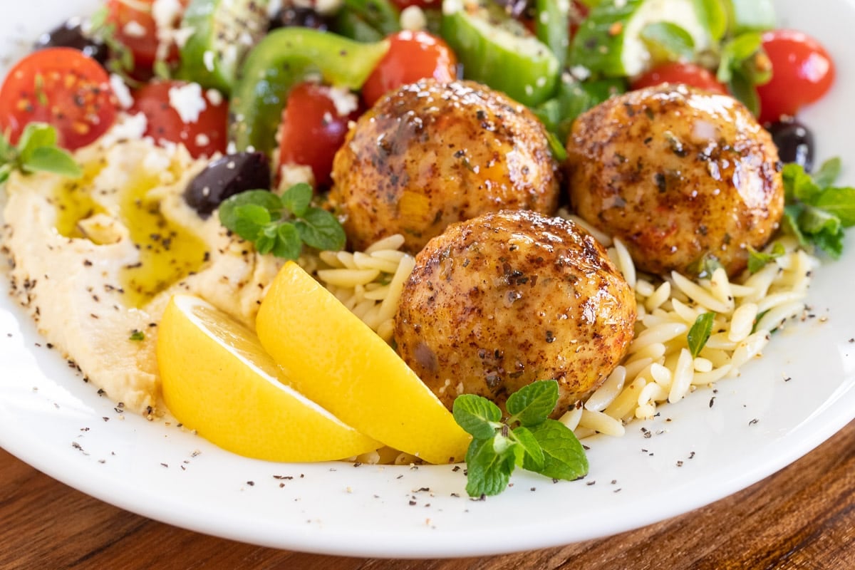 Horizontal closeup photo of Greek Chicken Meatballs with orzo, a Greek Tomato Cucumber Salad and hummus.