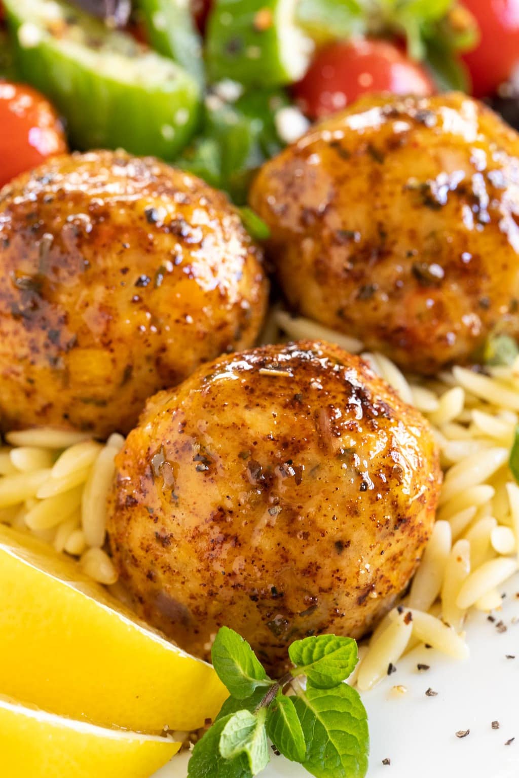 Vertical extreme closeup photo of Greek Chicken Meatballs on a bed of orzo with lemon wedges in the lower left corner.