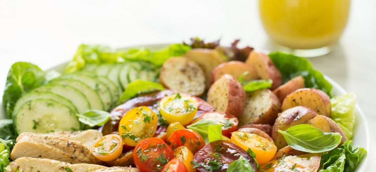 Vertical picture of Grilled Chicken with Tomato Cucumber Salad in a white bowl with a small jar of dressing in the background
