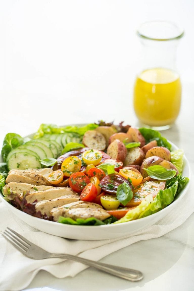 Vertical picture of Grilled Chicken with Tomato Cucumber Salad in a white bowl with a small jar of dressing in the background