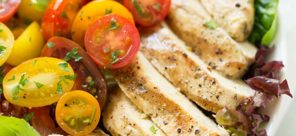 A horizontal photo of a white plate filled with a Grilled Chicken Tomato Cucumber Salad on a white granite counter.