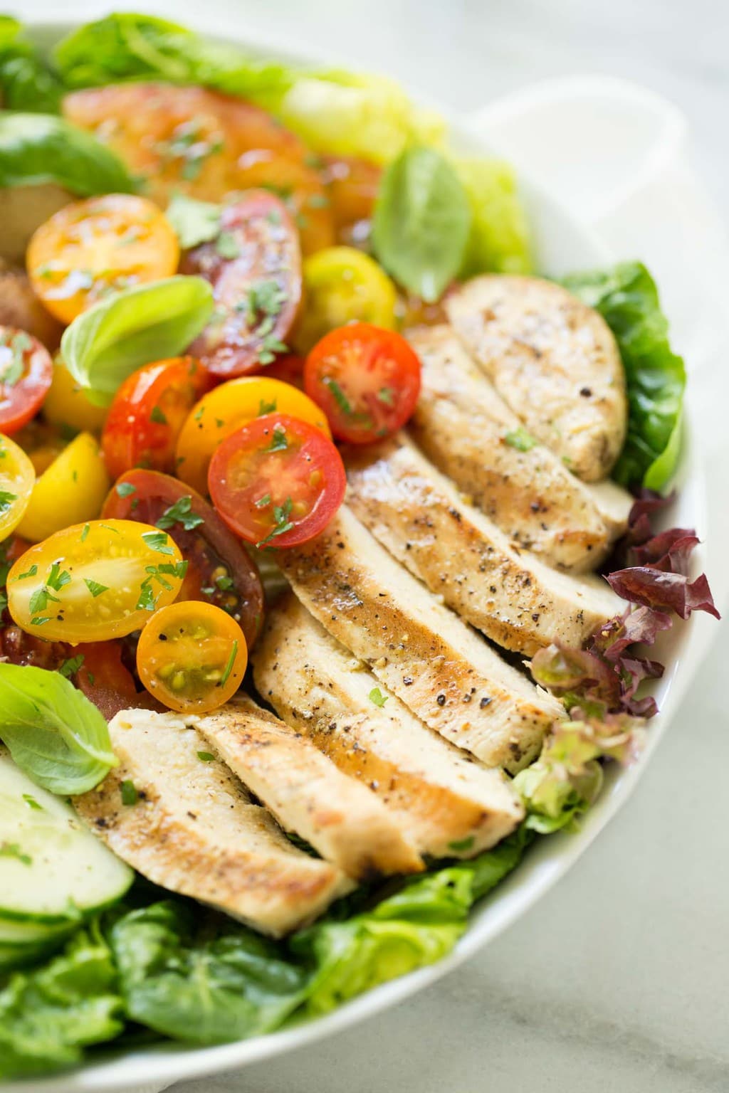 A horizontal photo of a white plate filled with a Grilled Chicken Tomato Cucumber Salad on a white granite counter.