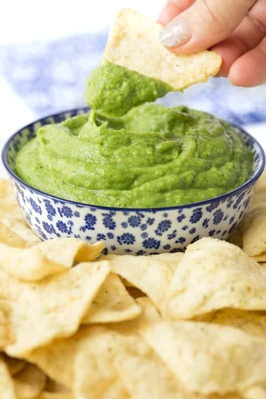 Vertical photo of a bowl of Guasacaca (Venezuelan Guacamol ) with a person's hand dipping a chip into the sauce.