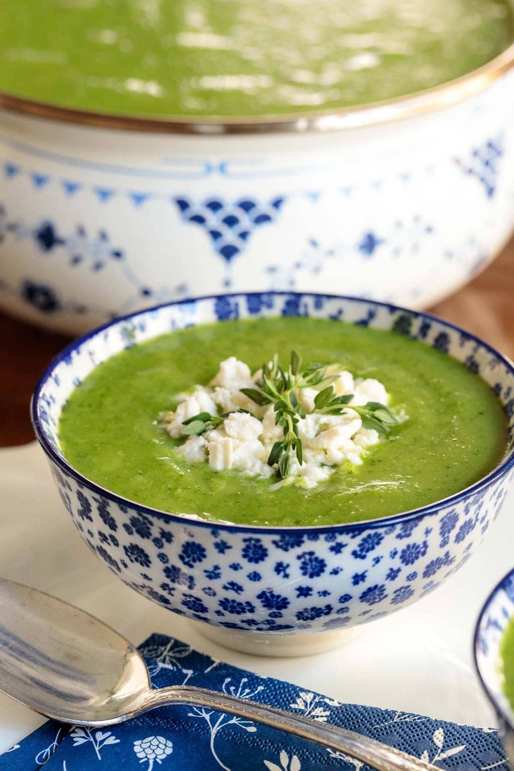 Vertical photo of Ham and Fresh Pea Soup in a blue and white patterned bowl with a pot of soup in the background.