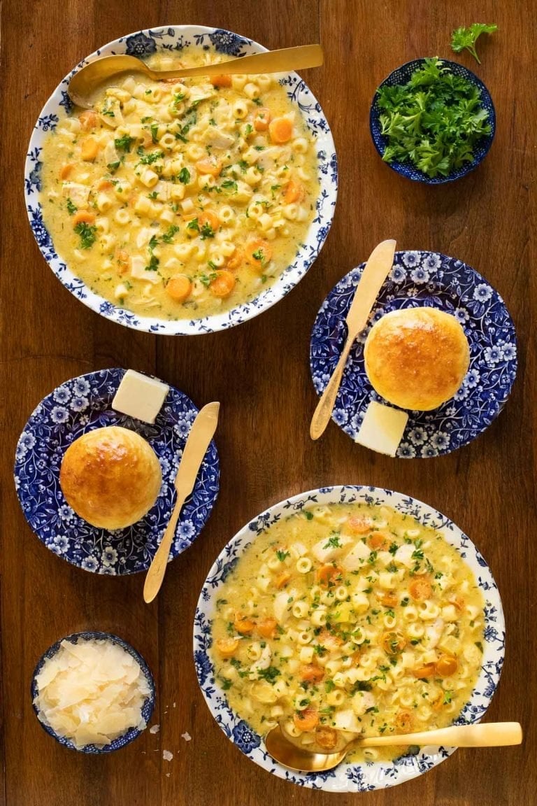 Overhead vertical photo of Creamy Chicken Pasta Soup in blue and white bowls on a wood table.