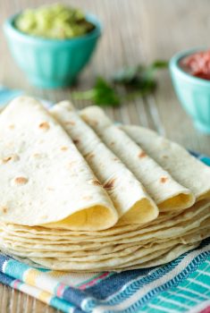 Horizontal photo of a stack of Homemade Flour Tortillas on a colorful kitchen towel.