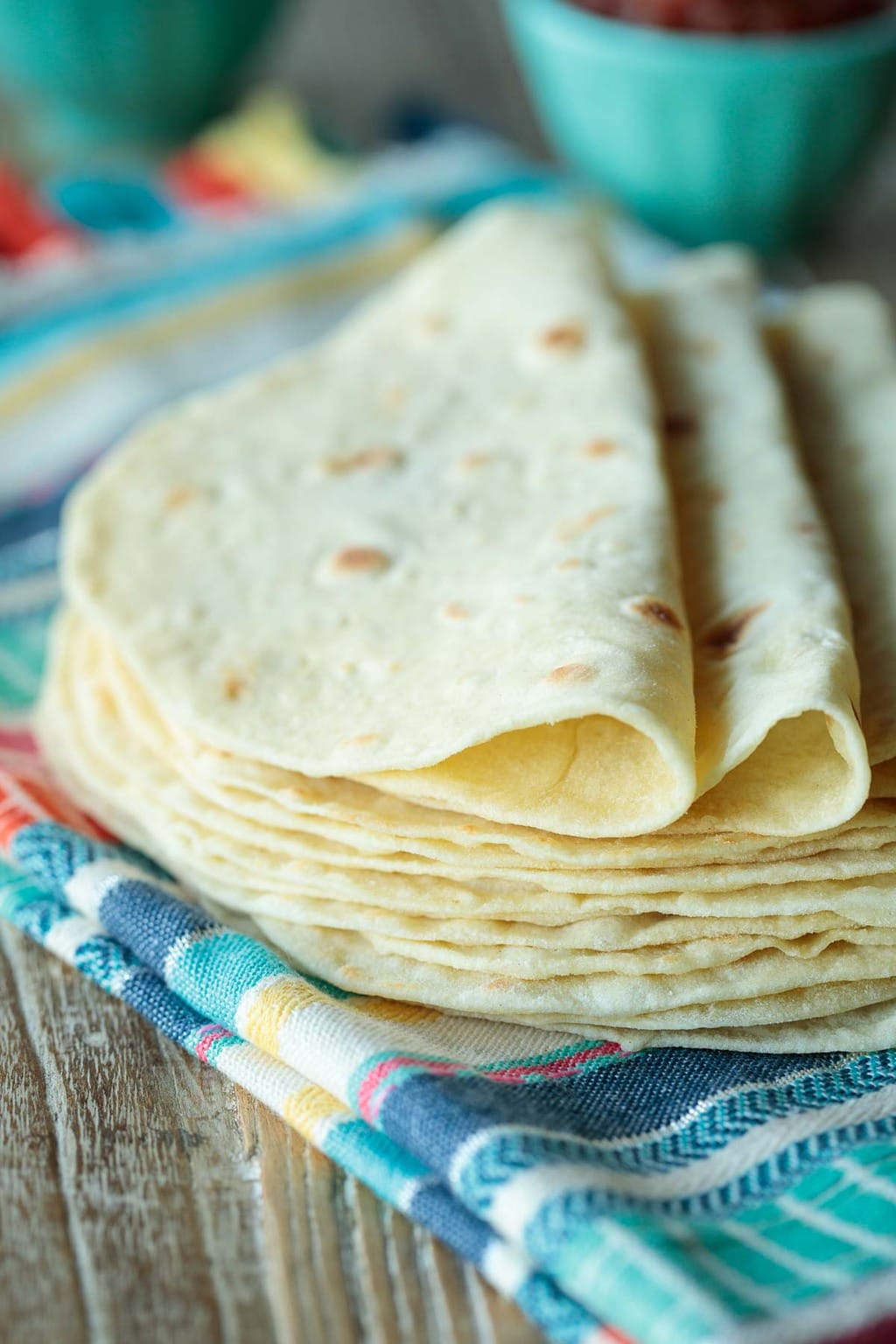 Photo of a stack of Homemade Flour Tortillas with two folded over each other on top.