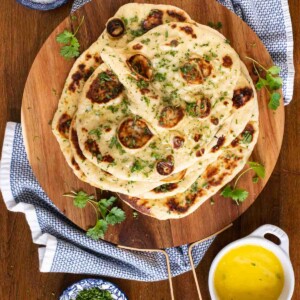 Overhead picture of homemade naan on a wooden cutting board with olive oil and herbs