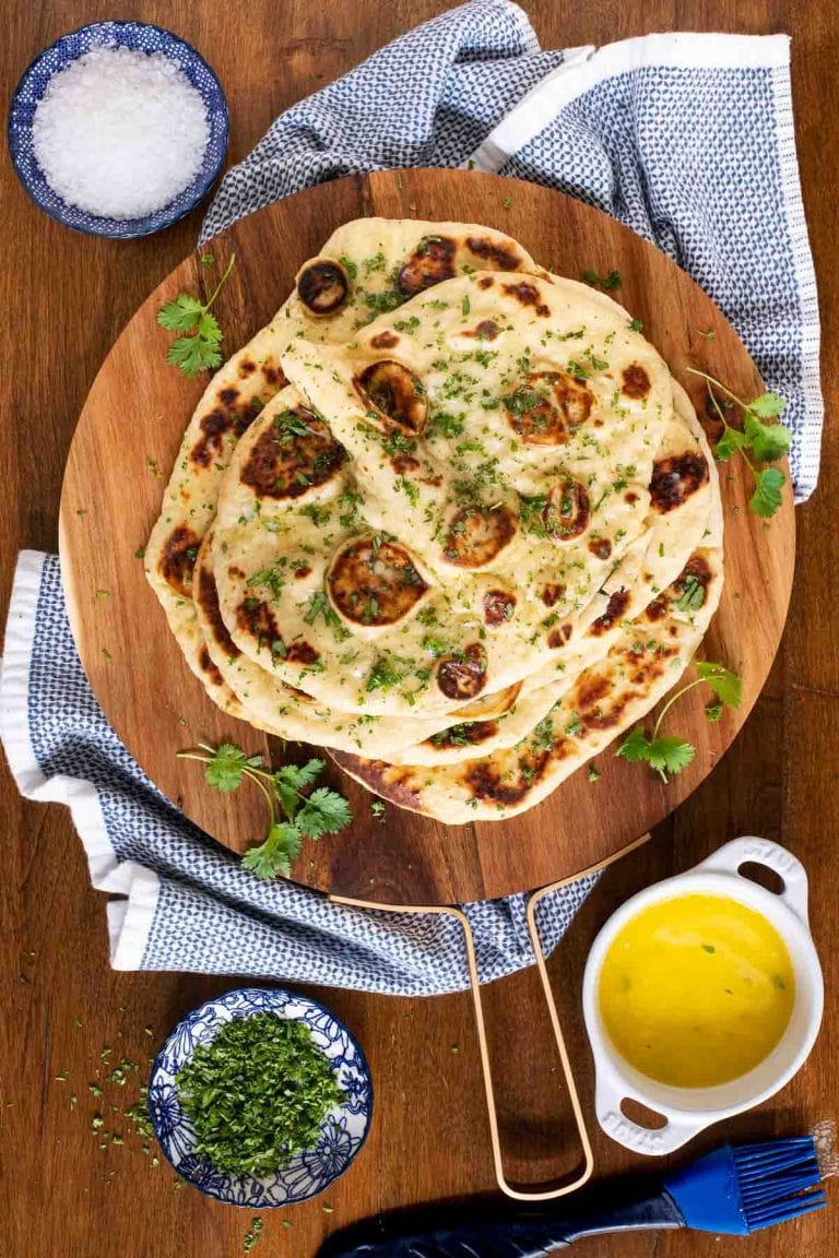 Overhead picture of homemade naan on a wooden cutting board with olive oil and herbs