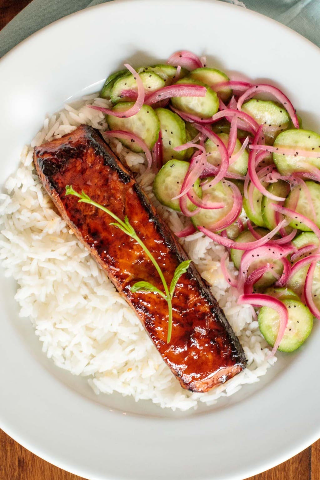 Overhead vertical photo of a Honey Coriander Make-Ahead Salmon with sliced cucumbers, red onions and resting on a bed of white rice..