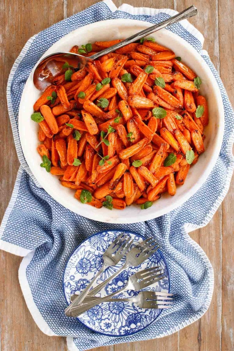 Overhead picture of Honey Ginger Charred Carrots in a white bowl on a blue and white towel with small plates and forks