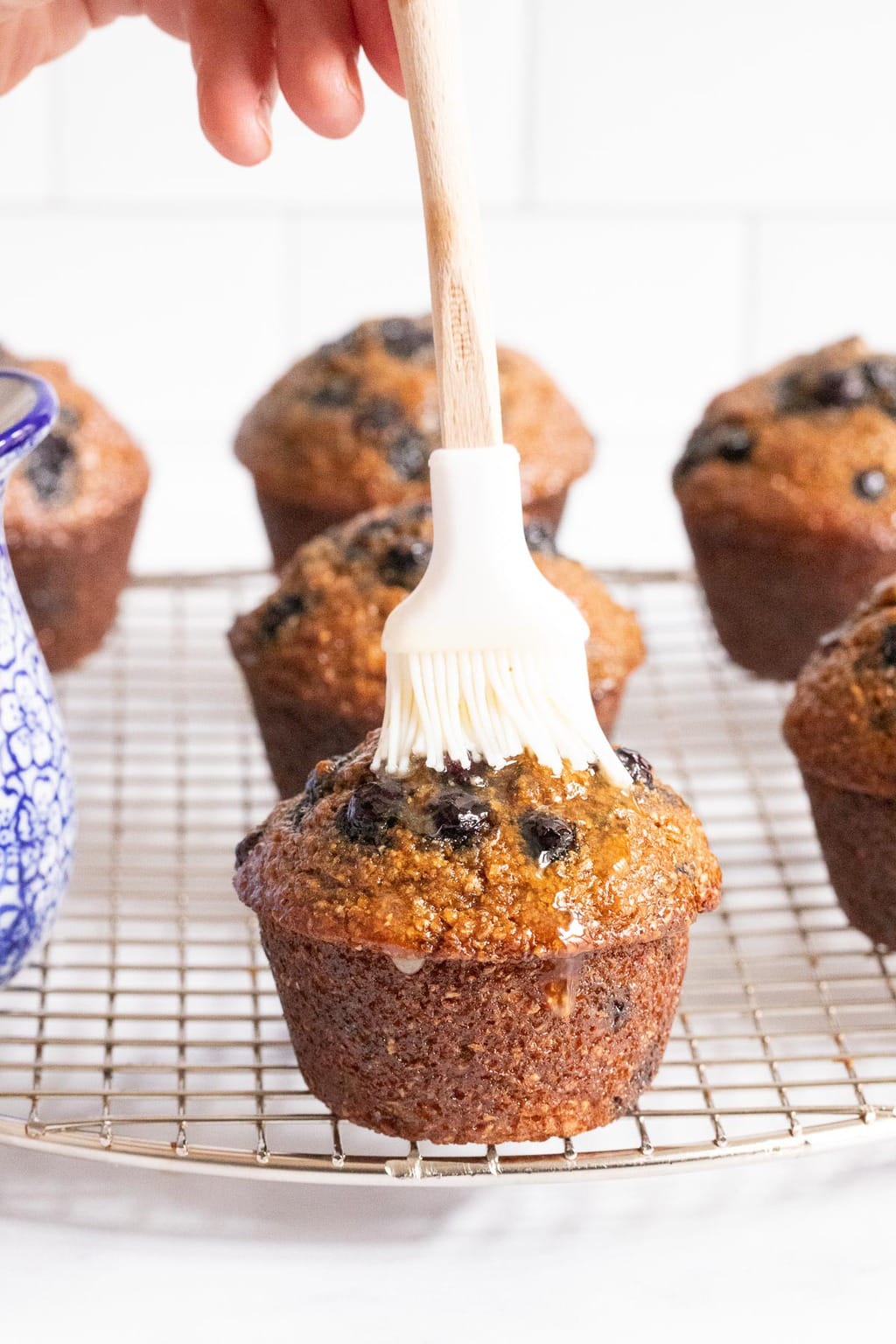 Vertical photo of a Honey-Glazed Blueberry Bran Muffin being brushed with honey glaze.