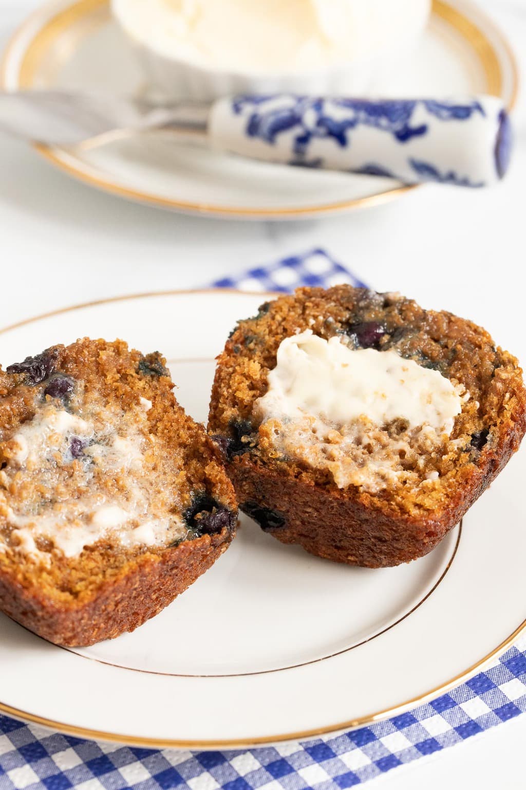 Vertical closeup photo of a Honey-Glazed Blueberry Bran Muffin opened and spread with melting butter.