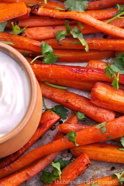 Closeup photo of a pan of honey roasted carrots with a dish of lemon tahini dressing in the middle of the pan.