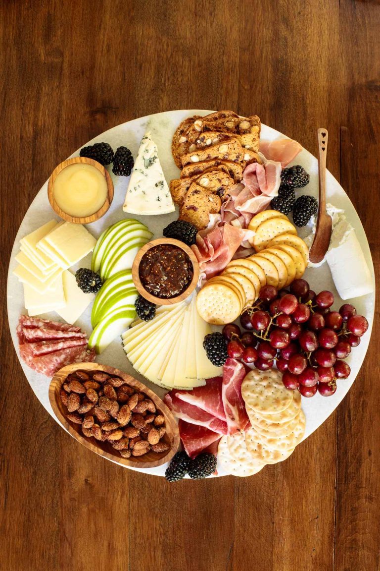 Overhead picture of a cheese board with crackers, fruit, jams, cheese and nuts on a wooden table