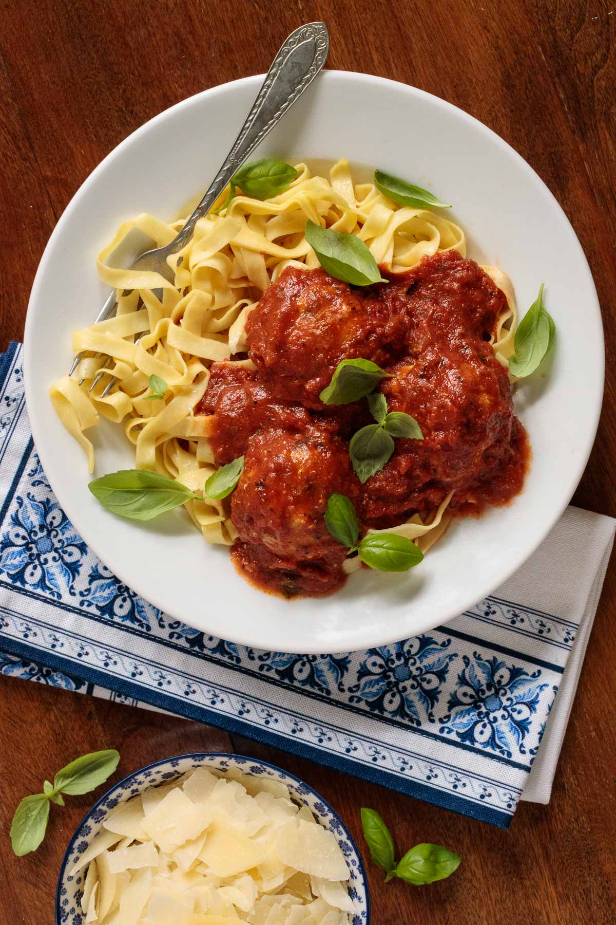 Overhead vertical photo of Italian Chicken Meatballs and Marinara with pasta and fresh basil in a white serving bowl.