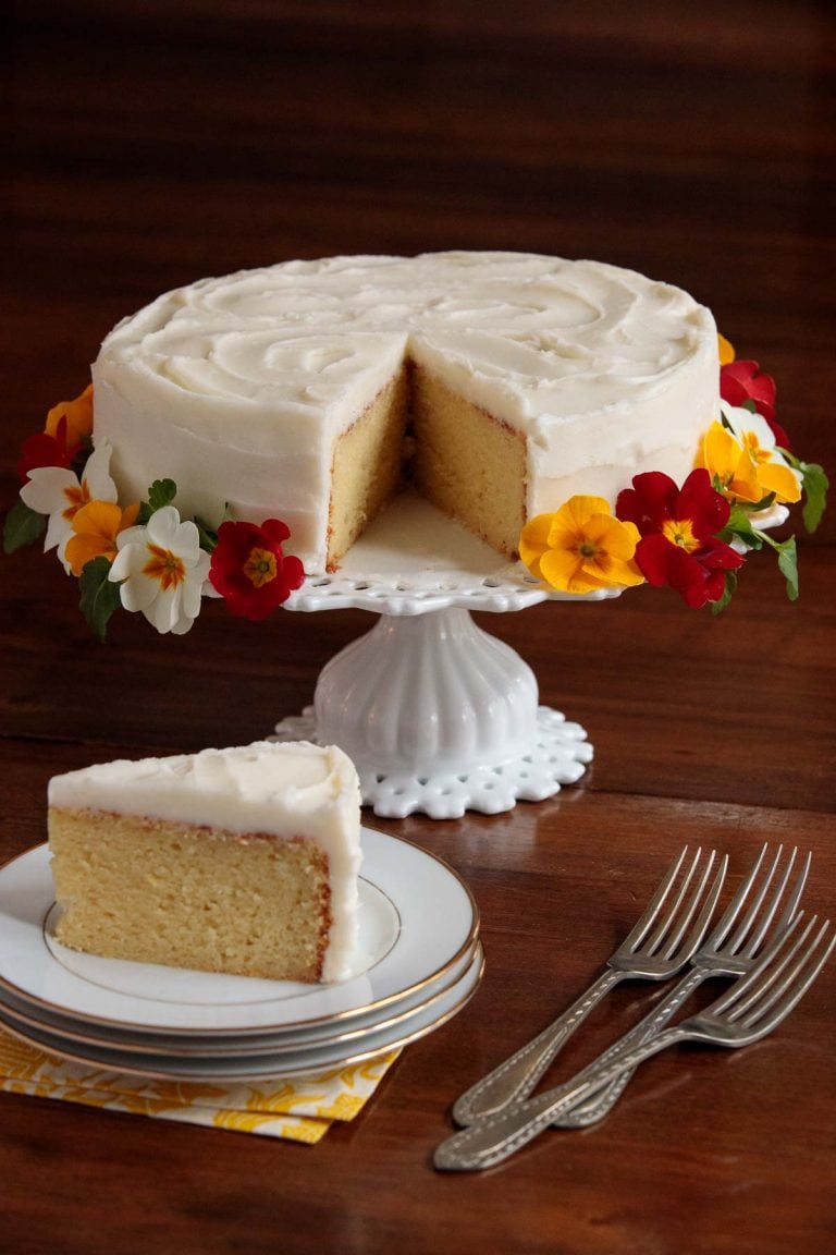 Vertical picture of Italian Lemon Ricotta Cake on a white cake stand with slice cut