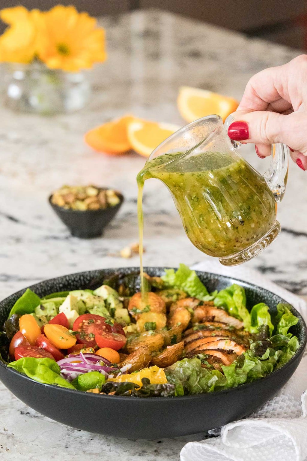 Horizontal photo of a person pouring dressing over a salad featuring Juicy Tender Restaurant Style Chicken Breasts in a black serving bowl on a granite countertop.