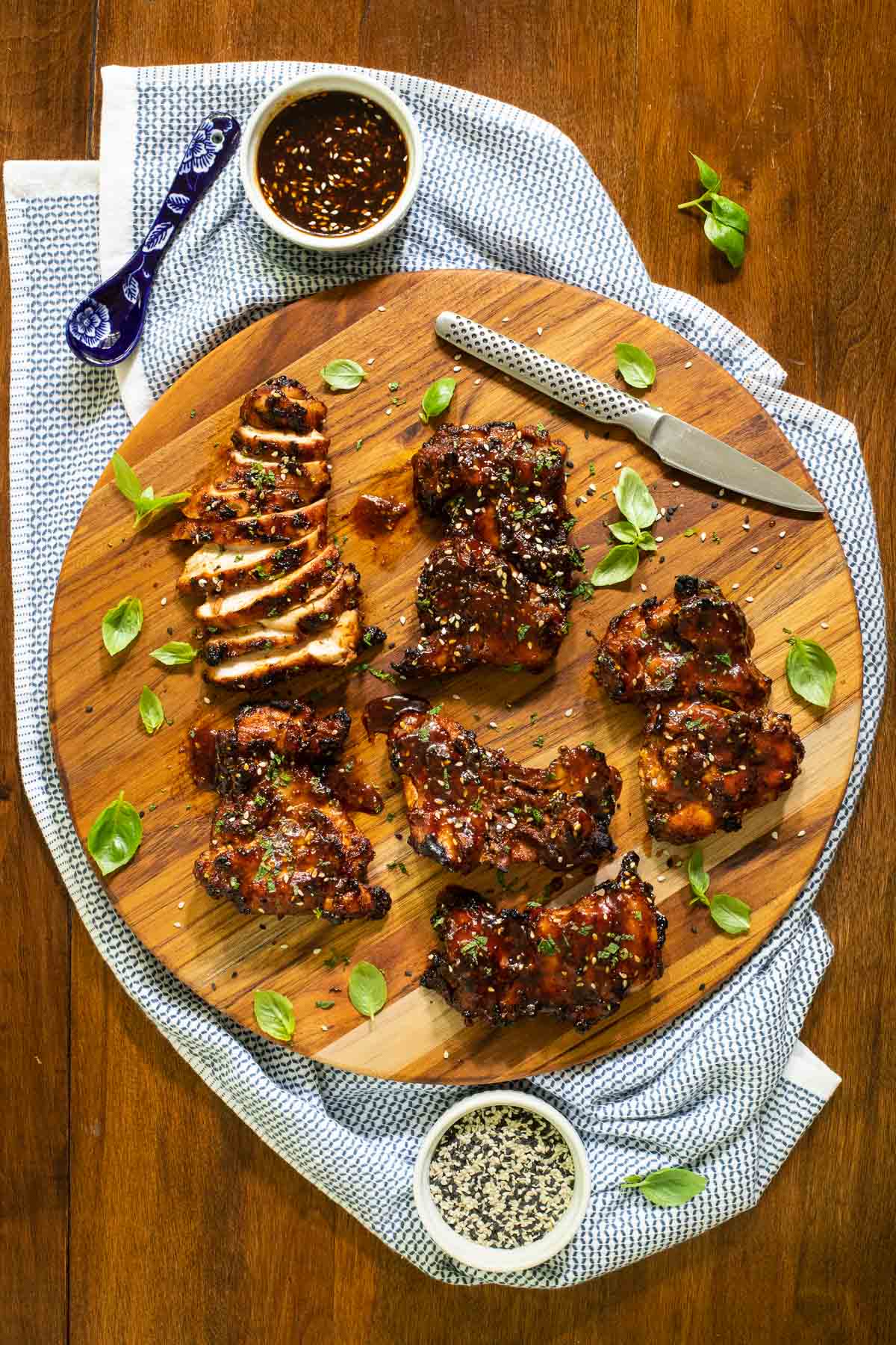 Overhead vertical photo of Korean Honey Sesame Grilled Chicken on a round wooden cutting board.
