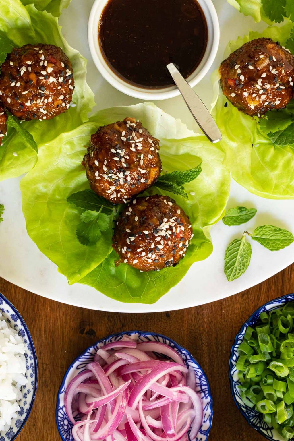 Overhead vertical closeup photo of Korean Meatball Lettuce Wraps with sauce and toppings.