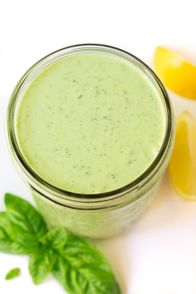 Closeup of a Ball jar filled with Lemon Basil Buttermilk Dressing and sprig of basil and lemon wedges leaning against the jar.