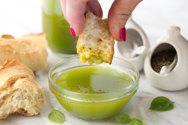 Photo of a glass dish of Lemon Basil Oil with a hand dipping crusty bread into the oil.