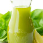 Vertical picture of Lemon Basil Oil in a glass jar with basil and lemons in the background