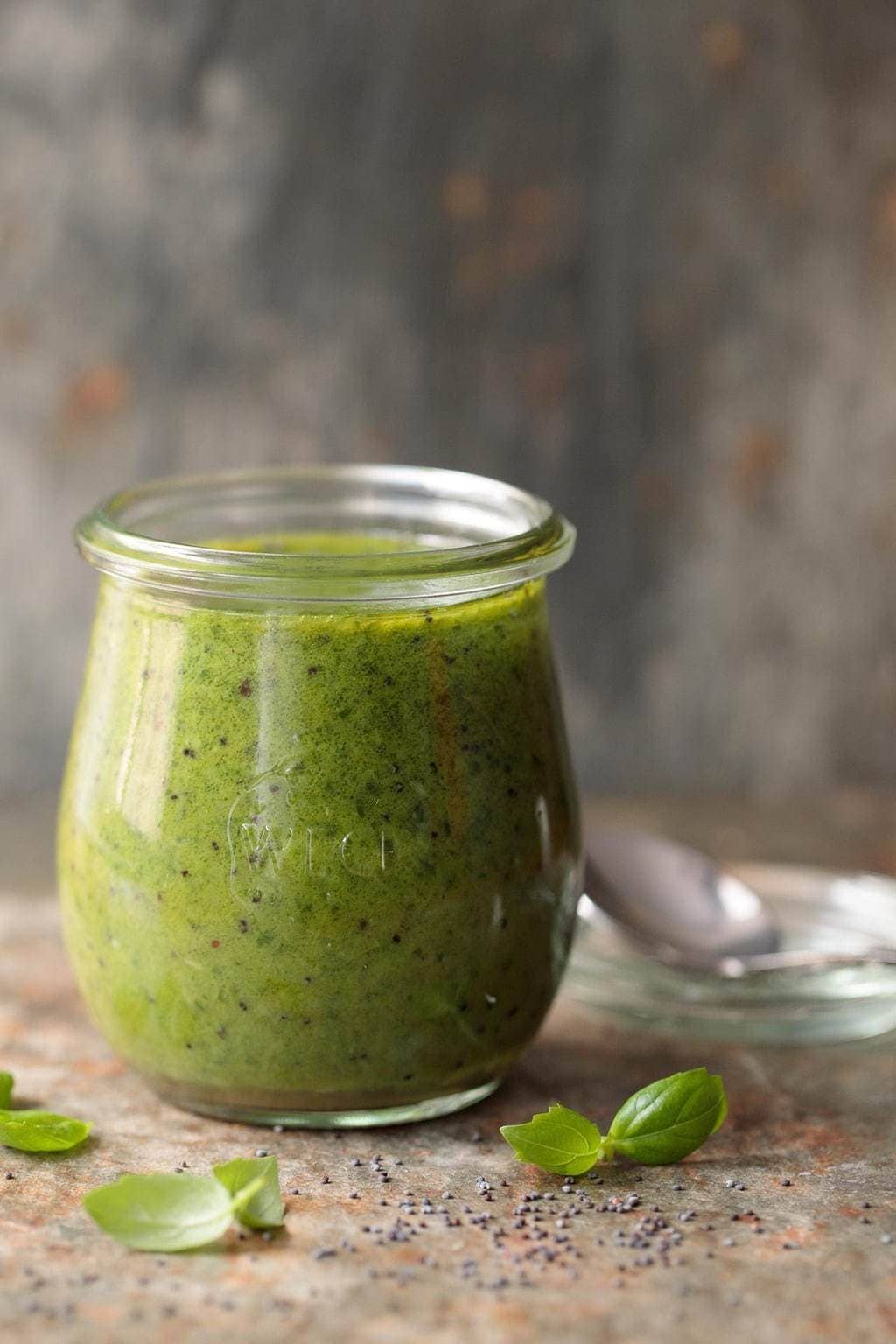 Photo of a Weck glass jar filled with Lemon Basil Poppy Seed Dressing on a slate surface with leaves of basil in the foreground.