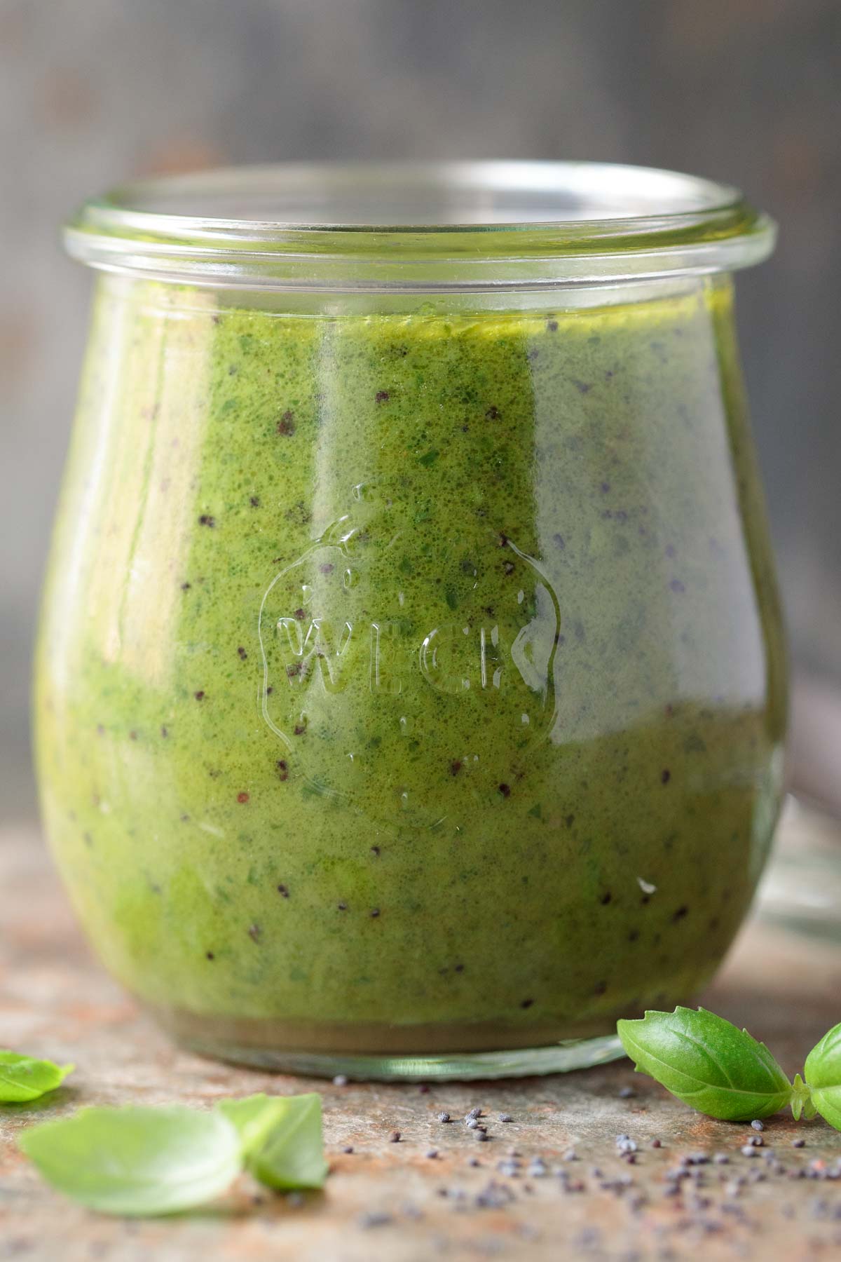 Vertical picture of Lemon Basil Poppyseed Dressing in a glass jar with fresh basil leaves