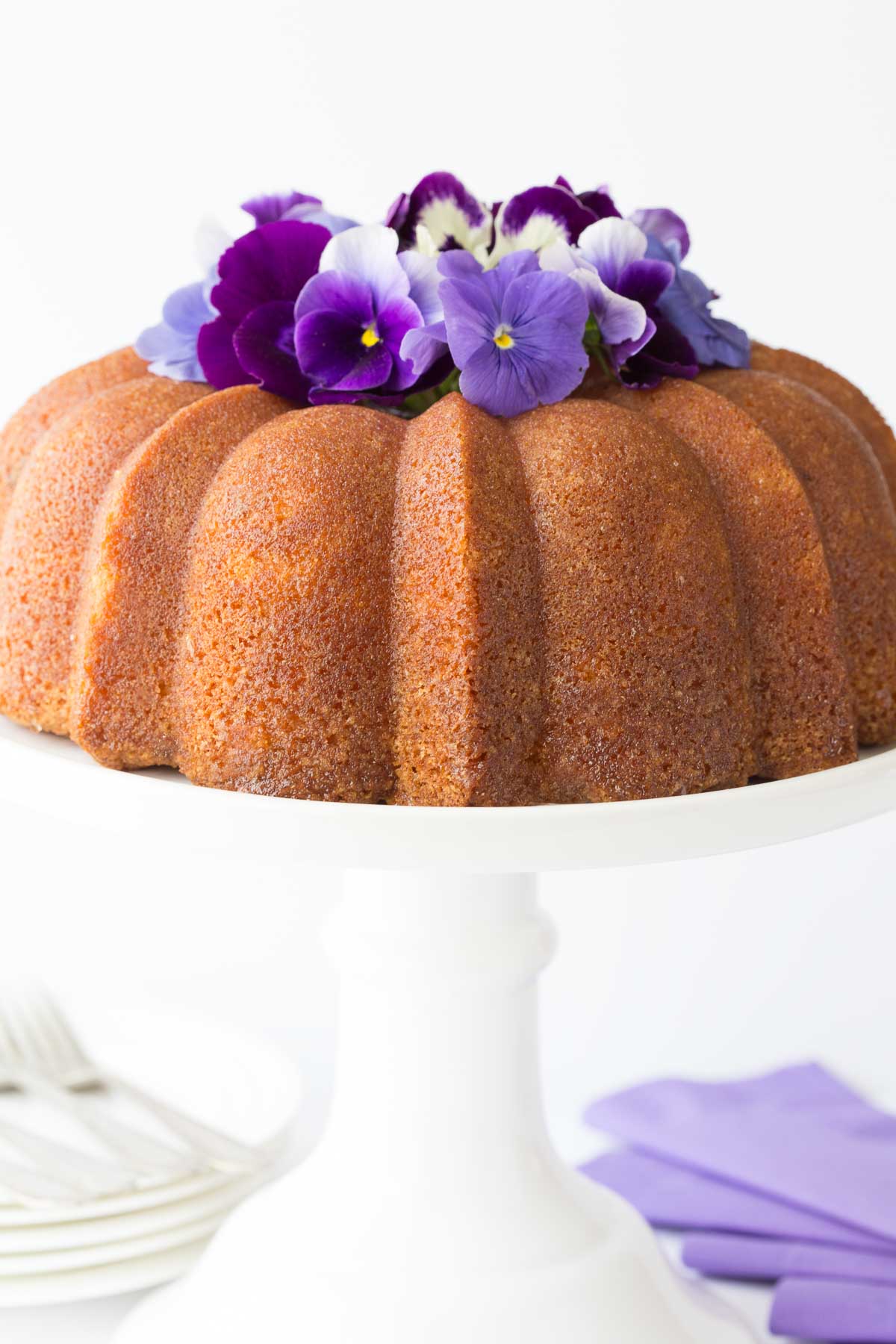 Vertical photo of a Lemon Buttermilk Pound Cake on a white cake stand 